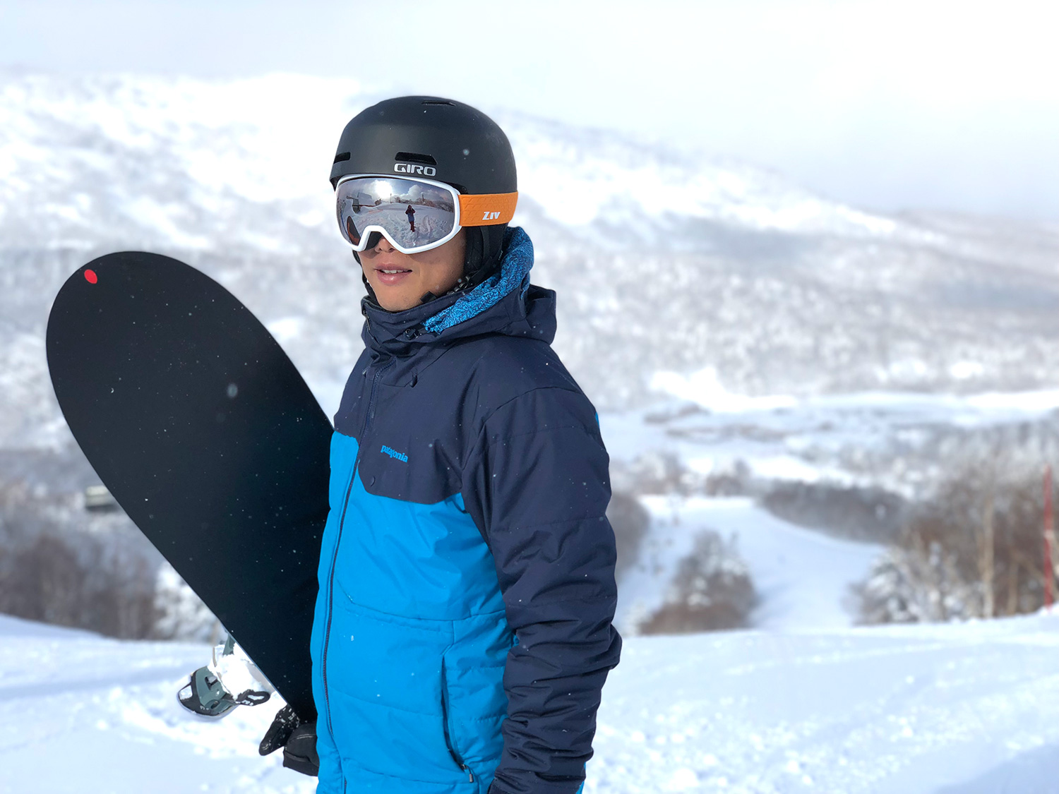 戴著ZIV雪鏡的年輕男孩，拿著雪板站在雪地裡